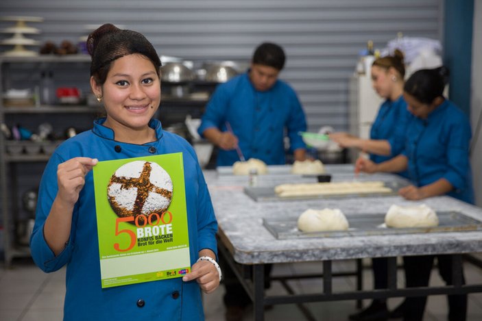 Bild zeigt ein junges Mädchen in einer Bäckerei die ein Plakat 5000 Brot hoch hält