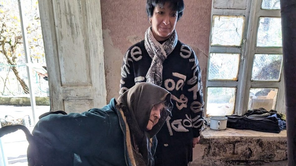 Bild zeigt eine alte Frau im Rollstuhl und eine jüngere die hinter ihr steht