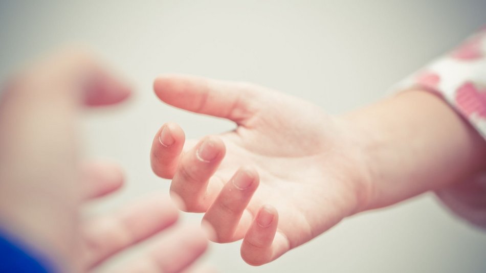 Bild zeigt eine Kinderhand die einer Erwachsenenhand entgegen gestreckt wird