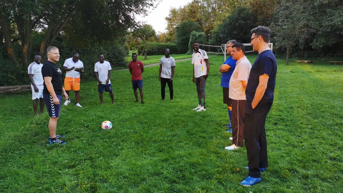 Mehrere Männer stehen auf einer grünen Wiese im Kreis.