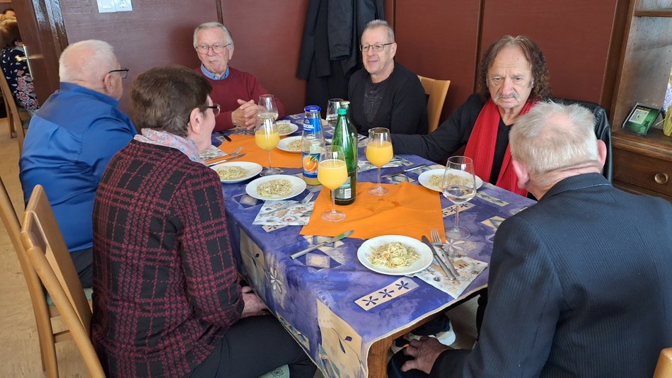 Bild zeigt mehrere Menschen die an einem gedeckten Tisch sitzen und sich unterhalten