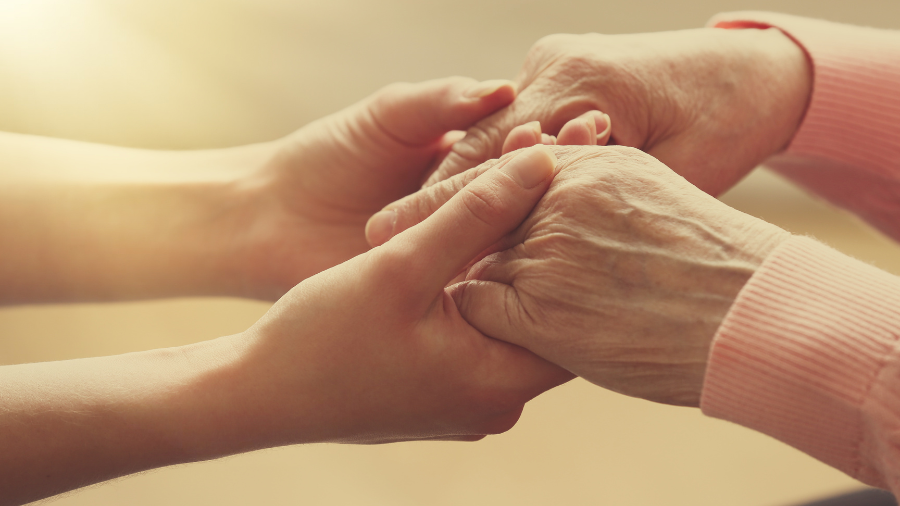 Zwei Paar Hände, eines von einer jüngeren Person und eines von einer älteren Person, greifen ineinander.