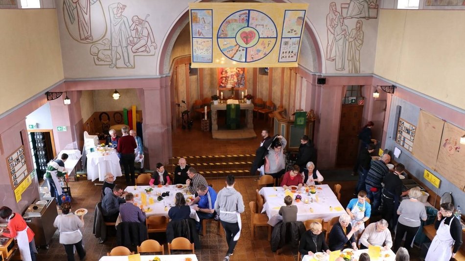 Innenraum einer Kirche mit Tischen und Menschen die essen.