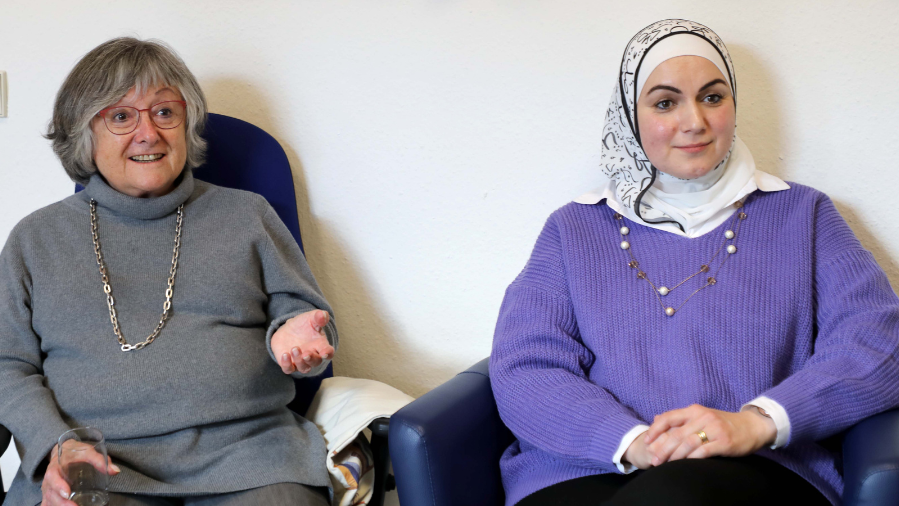 Zwei Frauen, eine mit und eine ohne Kopftuch, unterhalten sich mit jemandem außerhalb der Kamera.