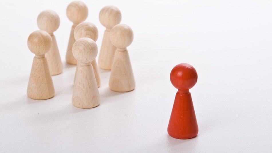 Bild zeigt Spielfiguren aus Holz, eine ist rot die anderen weiß