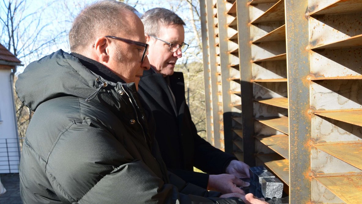 Zwei Männer legen drei kleine Gedenksteine in eine Wand