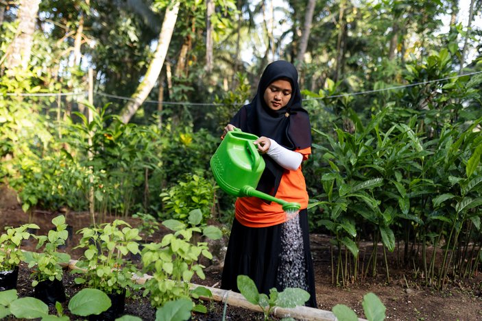 Eine Indonesische Frau gießt mit einer Gießkanne die Pflanzen.