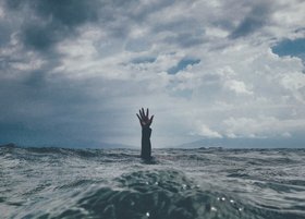 Eine Hand taucht aus einem stürmischen Meer auf.