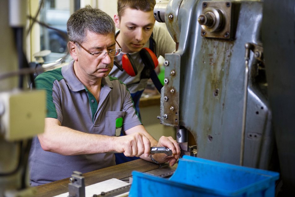 Zwei Männer arbeiten in einem Industriebetrieb an einer Maschine.