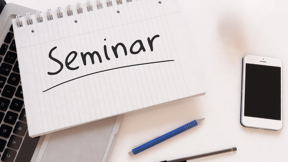 Auf einem Schreibblock steht in schwarz das Wort "Seminar". Unter dem Block liegt ein Laptop und daneben Stifte und ein Smartphone.