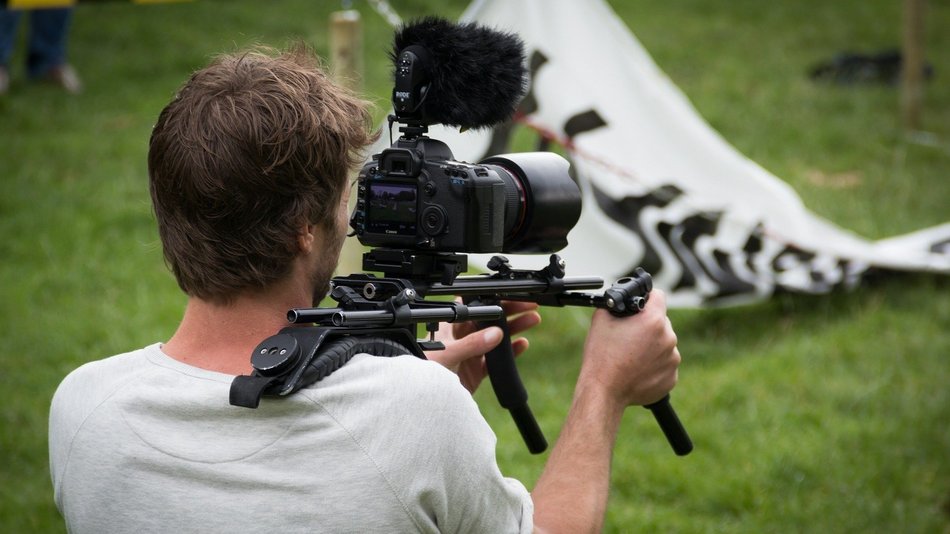 Bild zeigt einen Mann mit einer Kamera auf der Schulter