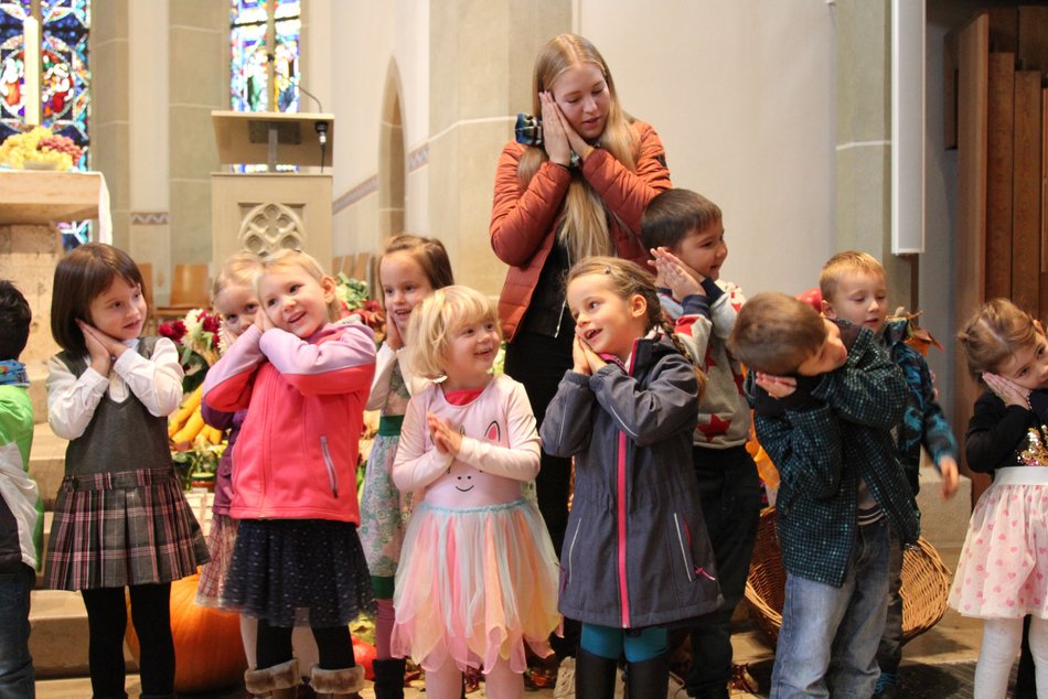 Das Bild zeigt mehrere Kinder mit einer Erwachsenen Person die vor dem Altar in der Kirche betende Hände an den Kopf halten