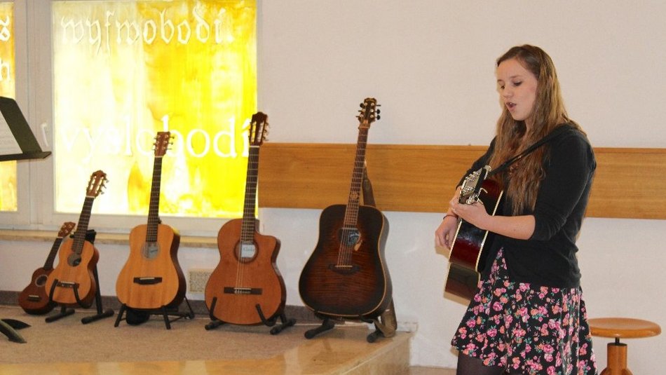 Bild zeigt eine Frau die auf ihrer Gitarre spielt im Hintergrund sind mehrere Gitarren zu sehen