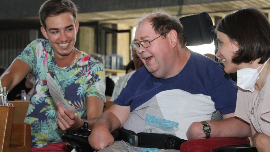 Ein Mann und eine Frau schauen zusammen mit einer Person mit Behinderung auf ein Blatt Papier.