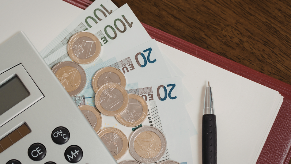 Neben einem Taschenrechner liegen ein paar Euro Münzen und zwei 20 Euro Scheine, zwei 100 Euro Scheine ein Schreibblock und ein Kugelschreiber.