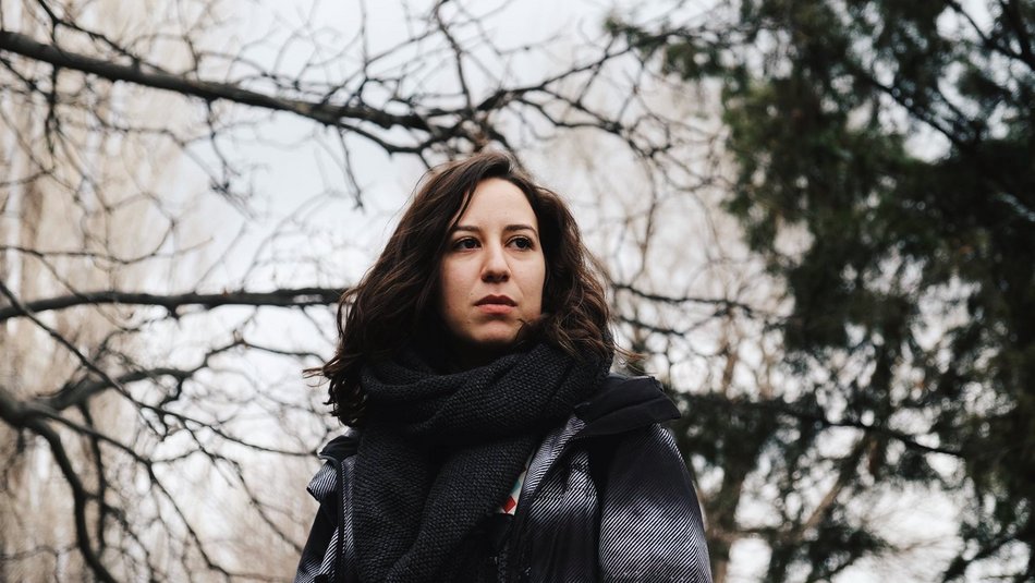 Eine Frau mit dunklen Haaren befindet sich im Freien und blickt in die Ferne.