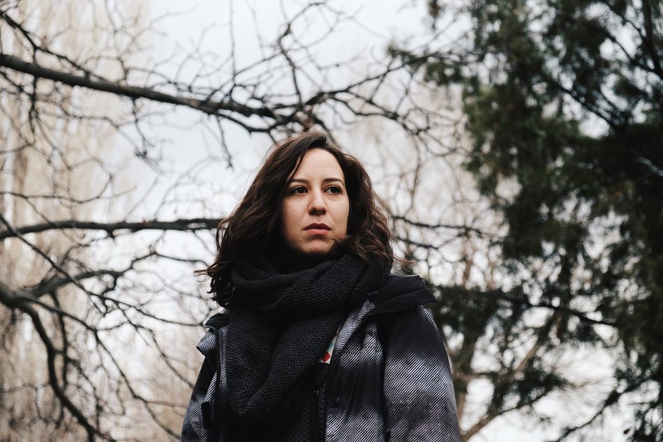 Eine Frau mit dunklen Haaren befindet sich im Freien und blickt in die Ferne.