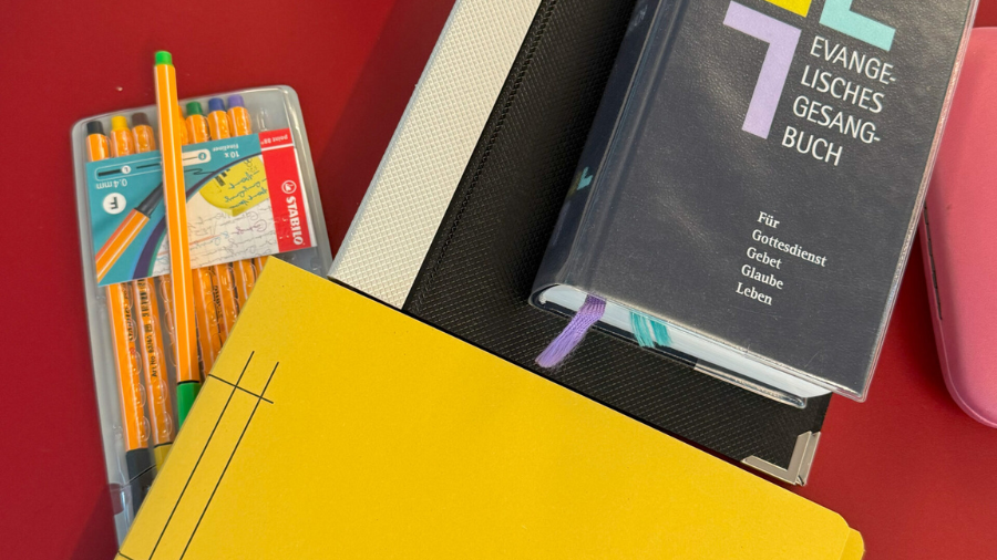 Ein Gesangbuch der Bibel, ein Notizbuch und Stifte sind zu sehen.