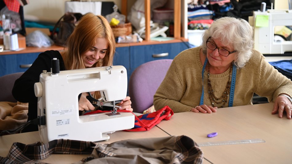 Bild zeigt zwei Frauen die an einer Nähmaschine zusammen arbeiten