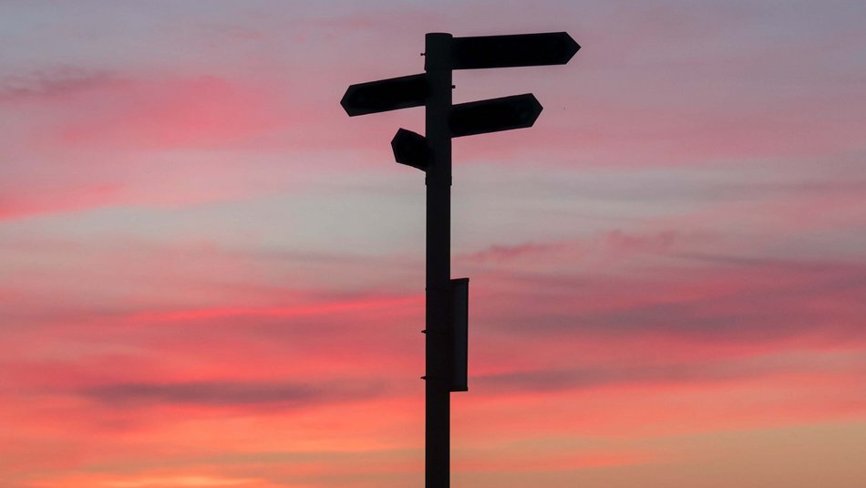 Bild zeigt eine Wegweiser der vor einem Sonnenuntergangshimmel steht