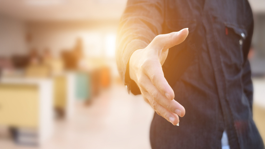 Eine Person streckt ihre Hand zur Begrüßung in die Kamera.