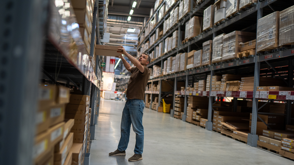 Ein Lagerarbeiter zieht ein Paket in einem großen Lager aus einem Regal.