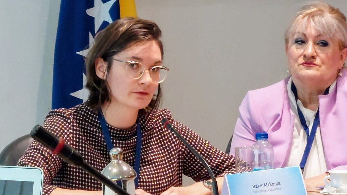 Eine Mitarbeiterin der Diakonie Württemberg spricht im Bosnischen Parlament an einem Tisch sitzend in ein Mikrofon. 