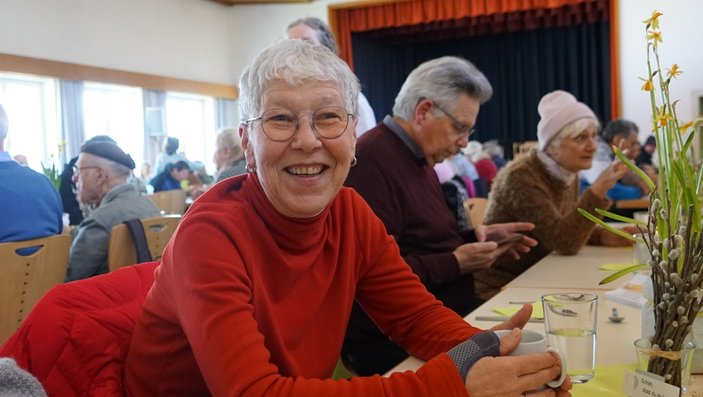 Bild zeigt eine Besucherin der Vesperkirche die am Tisch sitzt und in die Kamera lacht