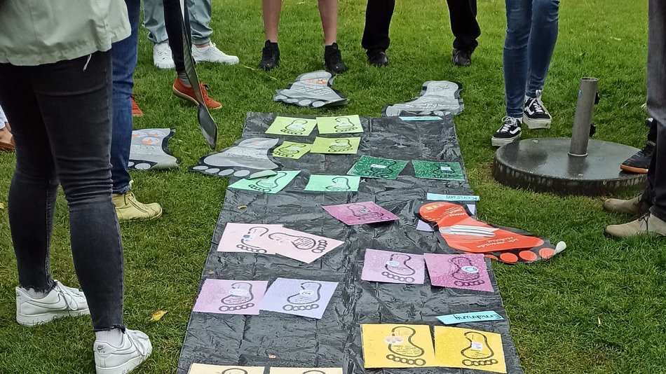 Bild zeigt bunte Füße auf Papier die auf einer schwarzen Folie liegen, die Füße sind mit Texten beschrieben