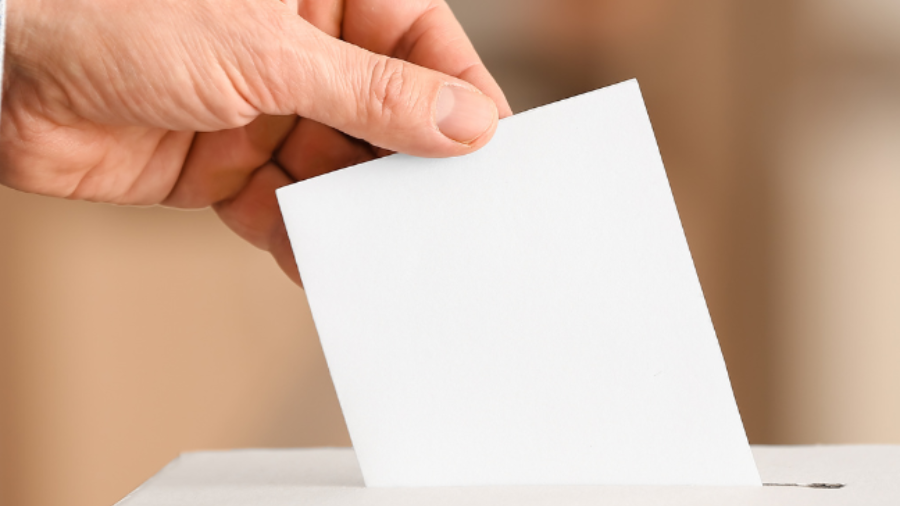 Eine Hand wirft einen Wahlzettel in eine Wahlurne.