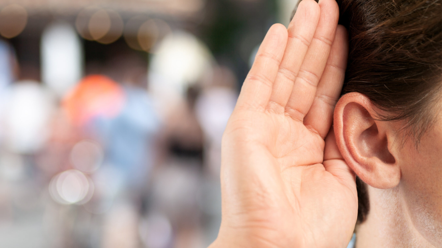 Eine Person hält sich die Hand ans Ohr, um besser zu hören.