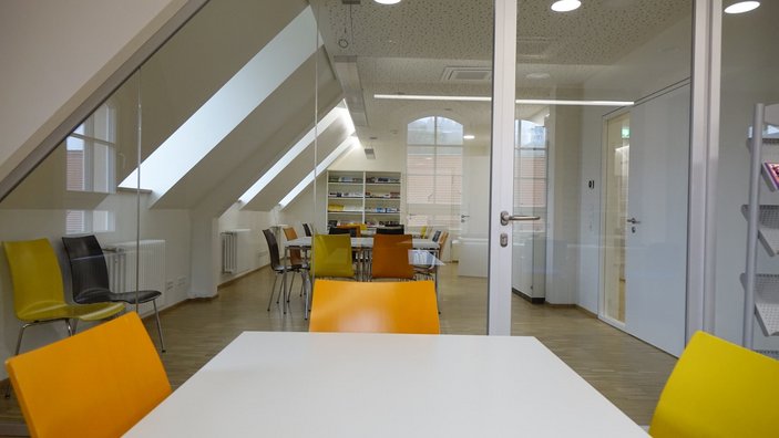 Es ist der ausgebaute Dachstuhl zu sehen in dem ein Tisch steht mit Stühlen.