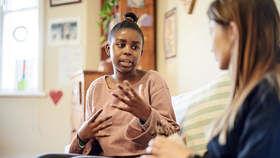 Eine Frau mit dunkler Hautfarbe sitzt auf einem Sofa und spricht mit einer Beraterin.