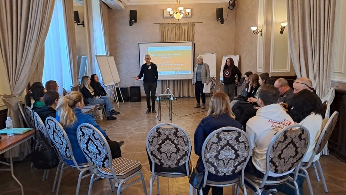 Ein Kreis mit Stühlen, auf dem Personen sitzen. In der Mitte steht eine Person und spricht.