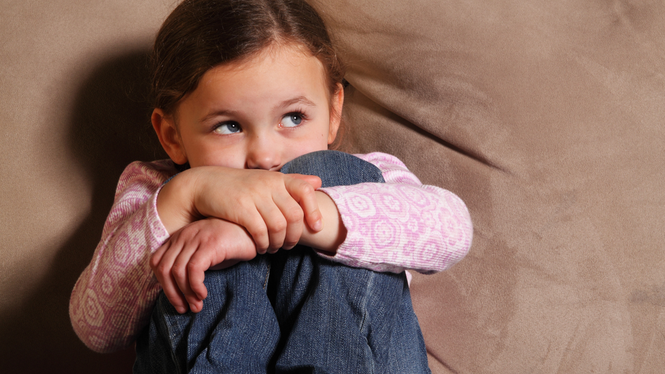 Ein kleines Mädchen sitzt ängstlich in einer Ecke.
