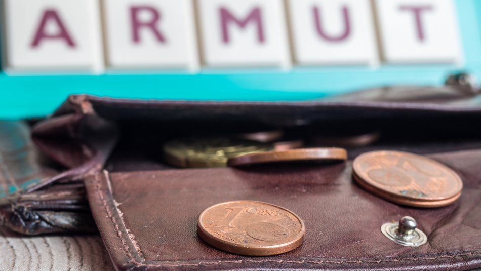 Vor dem Wort Armut liegt ein offener Geldbeutel mit wenigen Cent.