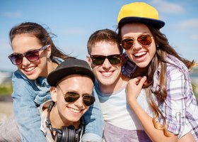Eine Gruppe Jugendlicher mit Sonnenbrillen lacht in die Kamera.