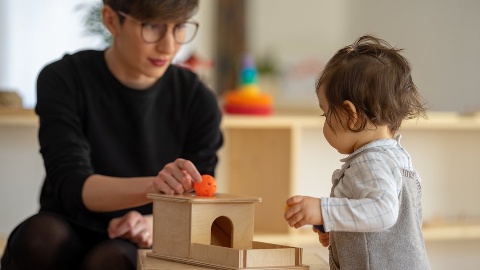 Bild zeigt eine junge Frau die mit einem Kind im Kindergarten spielt