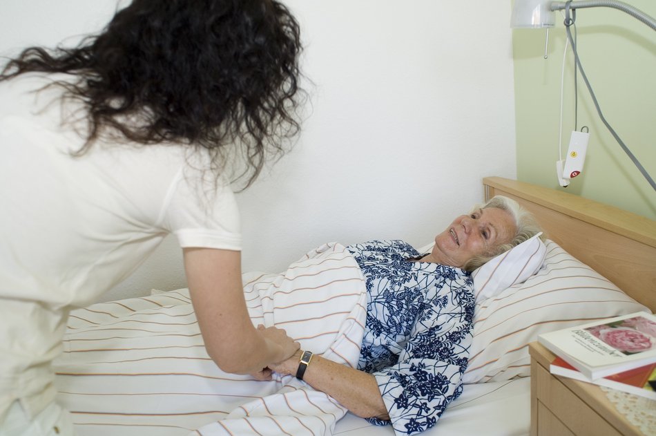 Bild zeigt eine Pflegerin am Bett einer älteren Dame