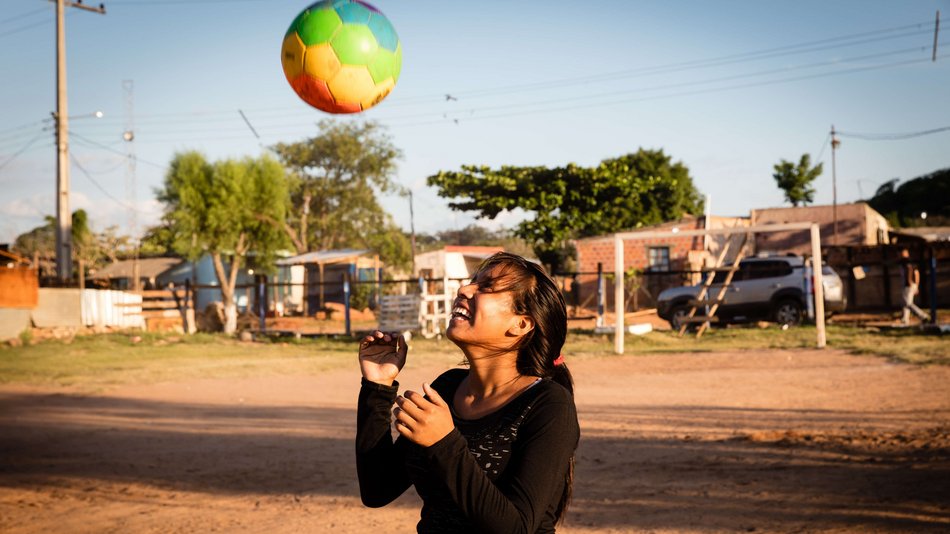 Bild zeigt eine junge Frau die einen Regenbogenfußball in die Höhe wirft