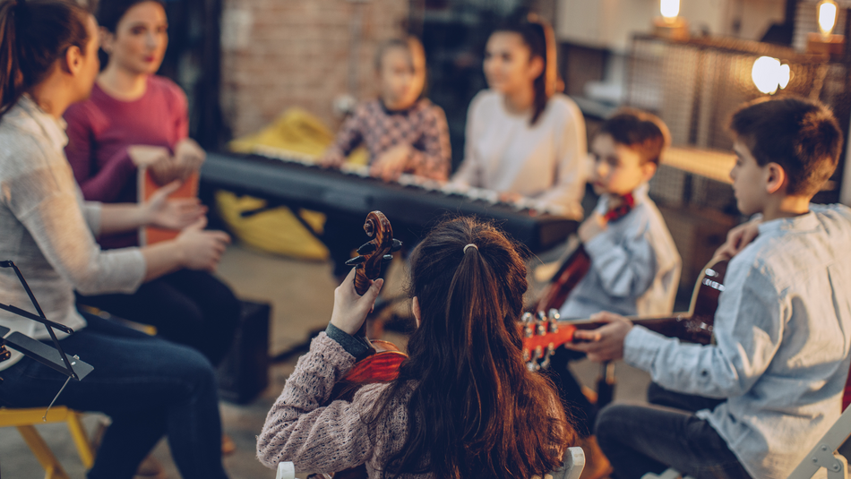 Mehrere Mädchen und Jungen sitzen in einem Raum im Kreis und machen Musik.
