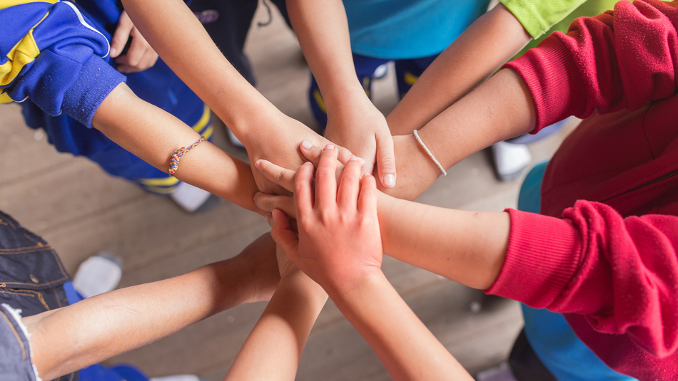 Die Hände von neun Kindern sind in der Mitte zu einem Kreis zusammengeführt.