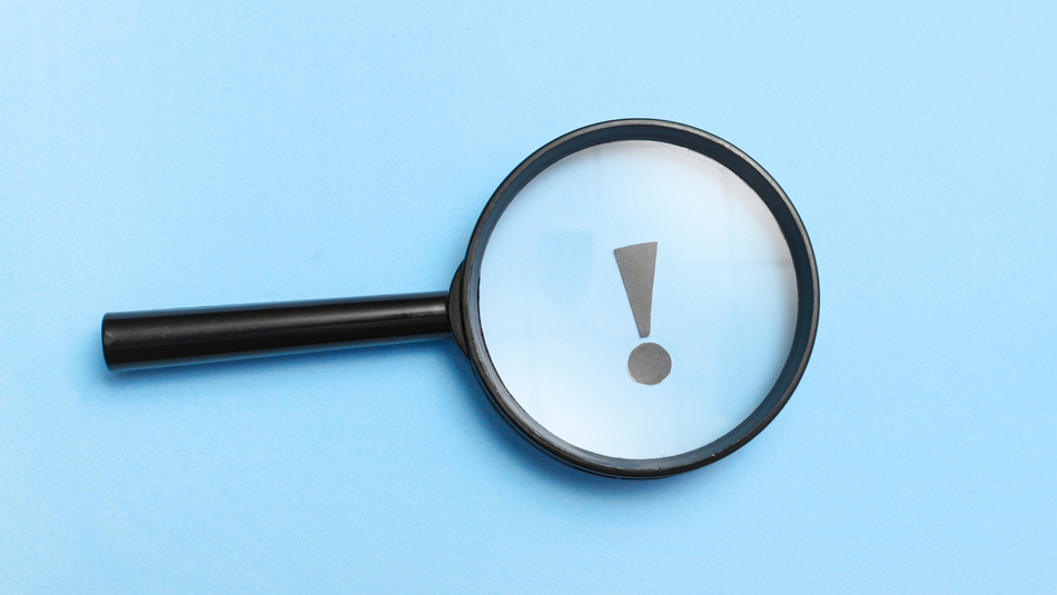 Ein Ausrufezeichen ist durch eine Lupe zu sehen. Der Hintergrund ist blau.