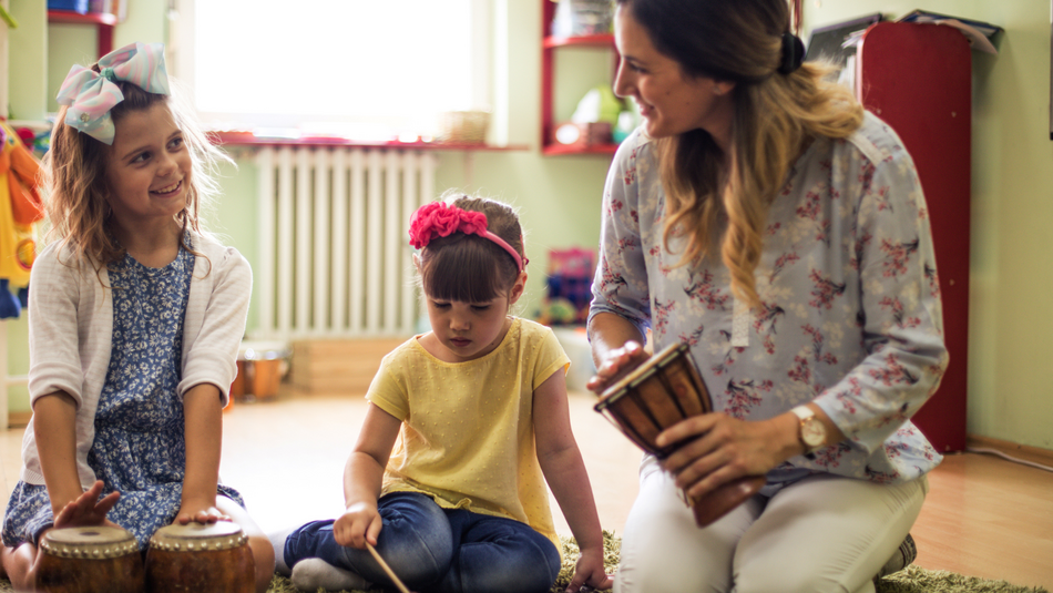 Eine Erzieherin spielt in einer Kindertageseinrichtung mit Kindern an Instrumenten.