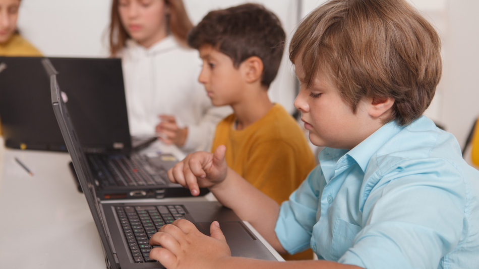 Kinder sitzen an einem Tisch und schauen in ein Laptop.