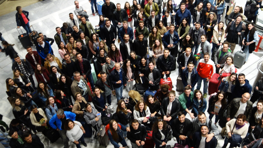 Von der Decke aufgenommenes Gruppenbild von vielen Personen, die am Flughafen ankommen.
