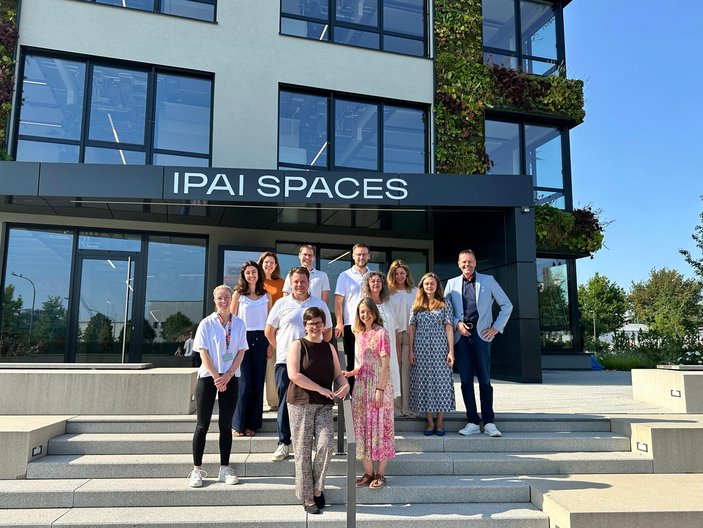 Eine Personengruppe steht in der Sonne vor einem Gebäude. Alle lachen in die Kamera.