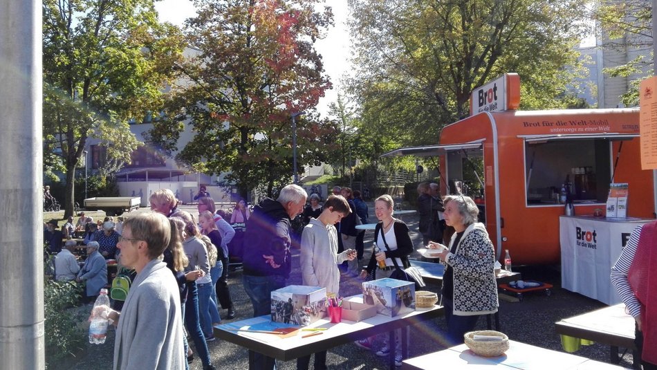Mehrere Menschen stehen im Freien vor dem orangenen Brot für die Welt-Mobil.