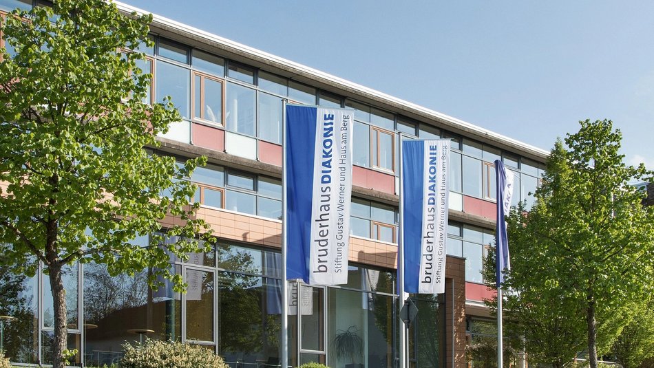 Zu sehen ist ein Gebäude der BruderhausDiakonie mit Fahnen des Logos davor.