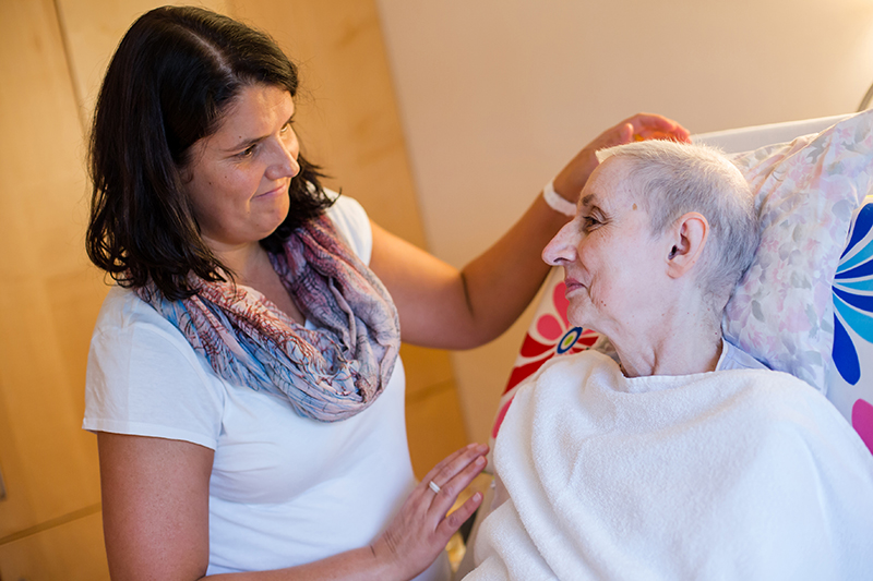 Bild zeigt eine sichtlich schwer erkrankte Frau im Hospiz die von einer Frau betreut wird
